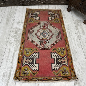 May include: A red, white, and brown patterned rug with a geometric design. The rug has a fringe border and is made of wool.