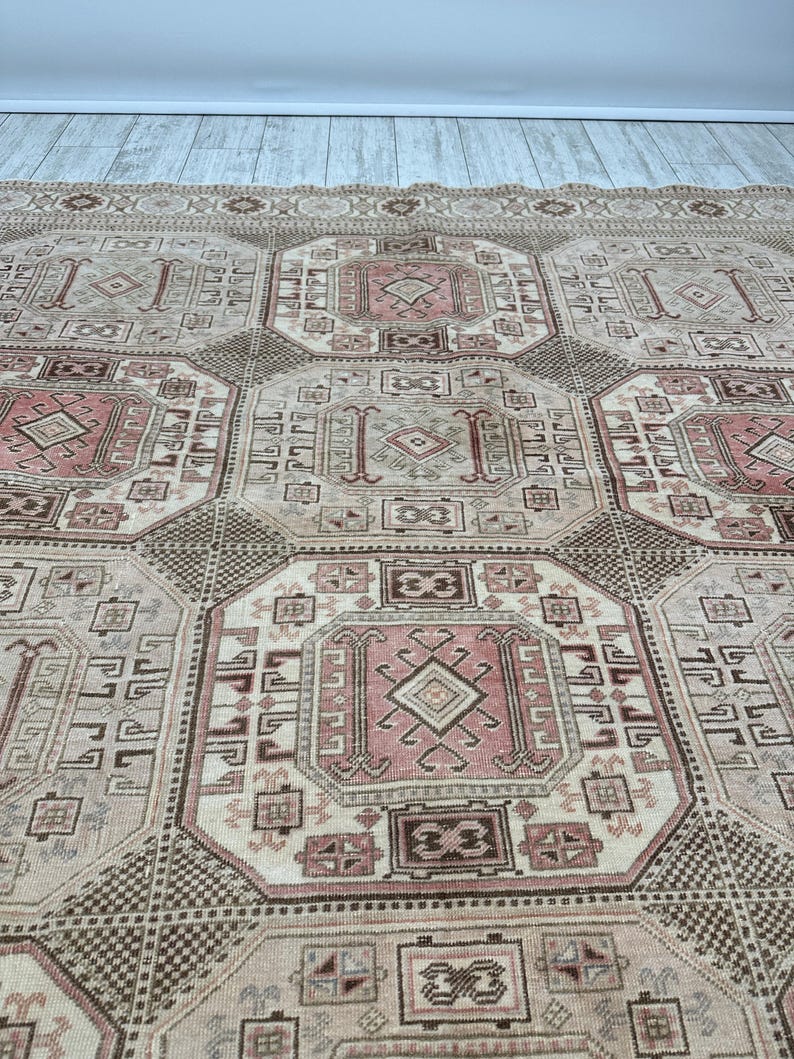 May include: A vintage rug with a geometric pattern in shades of beige, brown, and pink. The rug features a repeating design of squares and diamonds.