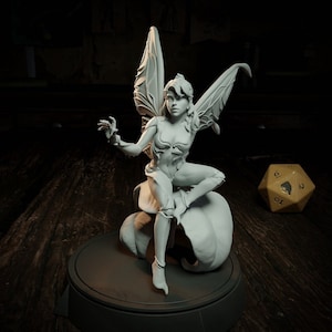 Peut inclure: Figurine grise détaillée d'une fée avec de grandes ailes ornées, assise sur une fleur stylisée. La fée est dans une pose dynamique, un bras tendu. Un grand dé à plusieurs faces est à l'arrière-plan.