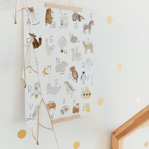 May include: A colorful alphabet poster with illustrations of animals and objects for each letter. The poster is hanging on a white wall with gold polka dots.