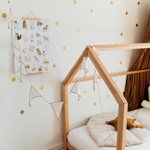 May include: A wooden house-shaped bed frame with a white mattress and a white and gold patterned rug. The wall behind the bed is decorated with gold polka dots and a white poster with an alphabet and animal illustrations.