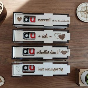 May include: Wooden boxes with the word "du" in red letters, and various phrases in German. The boxes are decorated with hearts and other designs. A wooden heart-shaped box, a compass, and keychains are also visible.