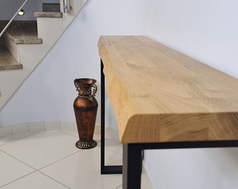 Puede incluir: Una mesa consola de madera con una tapa de borde vivo y patas de metal negro. La mesa está en un pasillo con una escalera en el fondo.