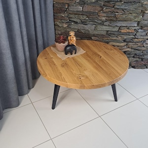 Könnte beinhalten: Ein runder Couchtisch aus hellem Holz mit schwarzen Beinen. Der Tisch hat ein natürliches Holzmaserungsmuster. Eine kleine Sukkulentenpflanze im Topf, ein Glas mit dekorativen Gegenständen und eine schwarze Elefantenfigur befinden sich auf dem Tisch.