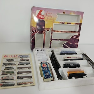 Könnte beinhalten: Ein Modelleisenbahn-Set von Lima mit einer Schachtel mit dem Markenlogo und einer Auswahl an Waggons, Gleisen und einem Netzteil. Ein Katalog mit Zugmodellen ist ebenfalls enthalten.