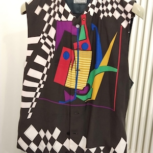 Puede incluir: Un chaleco negro con un diseño abstracto colorido. El chaleco presenta un patrón geométrico de cuadrados blancos y negros a cuadros en los lados y un diseño central con formas rojas, amarillas, azules y moradas. Está abotonado y colgado de una percha.