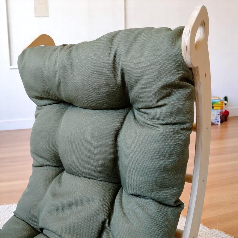 May include: A close-up of a green upholstered chair with a light wood frame. The chair has a tufted backrest and a rounded top. The frame has a ladder-like design. The chair is on a light-coloured rug.