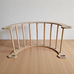 May include: A natural wood-coloured, curved wooden climbing arch with vertical dowels. The arch has a rounded base and two side platforms with holes. The design is simple and modern, suitable for children's play.