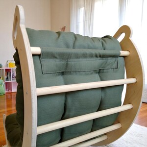 May include: A wooden rocking arch with a green cushion. The arch has a natural wood finish and features wooden dowels for climbing. The green cushion is tufted and provides a comfortable seat. The design is suitable for children.