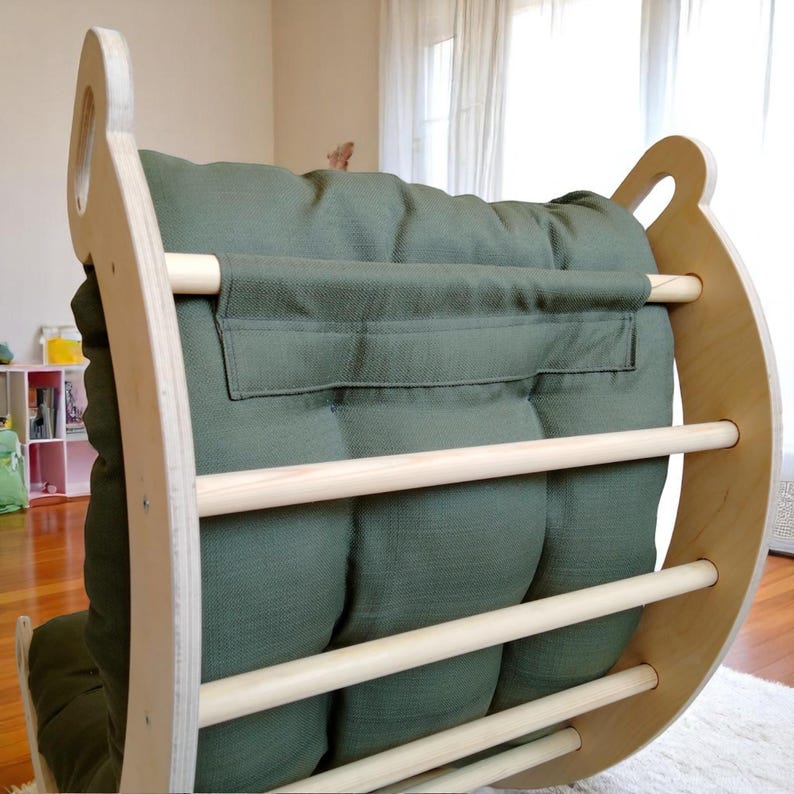 May include: A wooden rocking arch with a green cushion. The arch has a natural wood finish and features wooden dowels for climbing. The green cushion is tufted and provides a comfortable seat. The design is suitable for children.