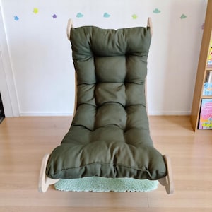 May include: A green cushioned rocking chair with a wooden frame. The chair has a high back and a tufted design on the seat and backrest. The chair is on a small green rug.