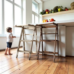 May include: Two wooden step stools, one light and one dark, stand side-by-side. Each has a rectangular top and three steps. A child stands nearby, observing the stools. The setting is a kitchen, with a shelf displaying fruit and vegetables.