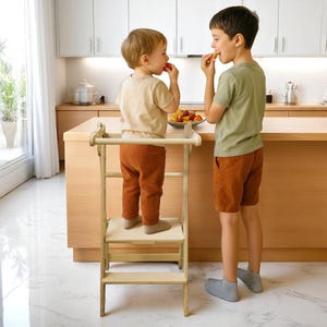 Può includere: Uno sgabello da cucina in legno chiaro con una barra di sicurezza. Due bambini sono in piedi vicino a un bancone della cucina, mangiando frutta. Lo sgabello ha due gradini e una piccola piattaforma. I bambini indossano abiti casual.