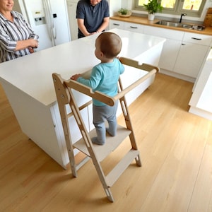 May include: A wooden toddler step stool with a safety rail. The step stool has a platform for the child to stand on and a bar for them to hold. Designed to help a child reach kitchen worktops, the stool is made of natural wood.