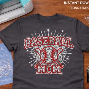 Puede incluir: Camiseta gris oscuro con un diseño de pedrería. El diseño presenta las palabras "BASEBALL MOM" en pedrería roja, con una pelota de béisbol en el centro. La camiseta está sobre una superficie de madera con una máquina Cricut y un archivo SVG azul.
