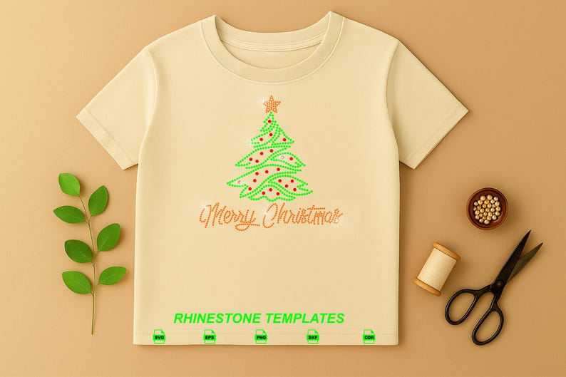 May include: A beige short-sleeved t-shirt featuring a rhinestone graphic of a green Christmas tree with red accents and a star topper. Below the tree, the text Merry Christmas is written in rhinestones. The words RHINESTONE TEMPLATES appear at the bottom.