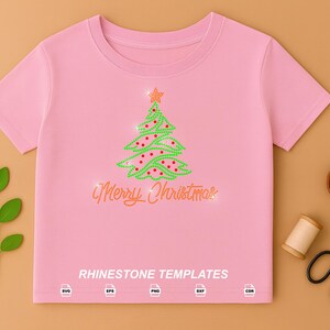 May include: A light pink short-sleeved t-shirt featuring a rhinestone Christmas tree design with a star topper and the text Merry Christmas in script. Below the text, the words RHINESTONE TEMPLATES appear with five file format icons.