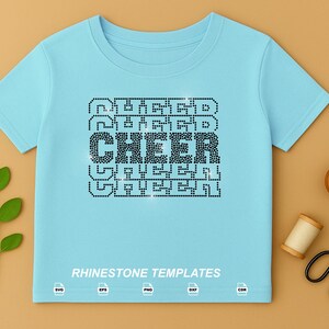 May include: A light blue short-sleeve t-shirt featuring a central graphic design made of black rhinestones that spells out the word CHEER in a repeating stacked pattern. The text RHINESTONE TEMPLATES is printed in white at the bottom of the shirt.
