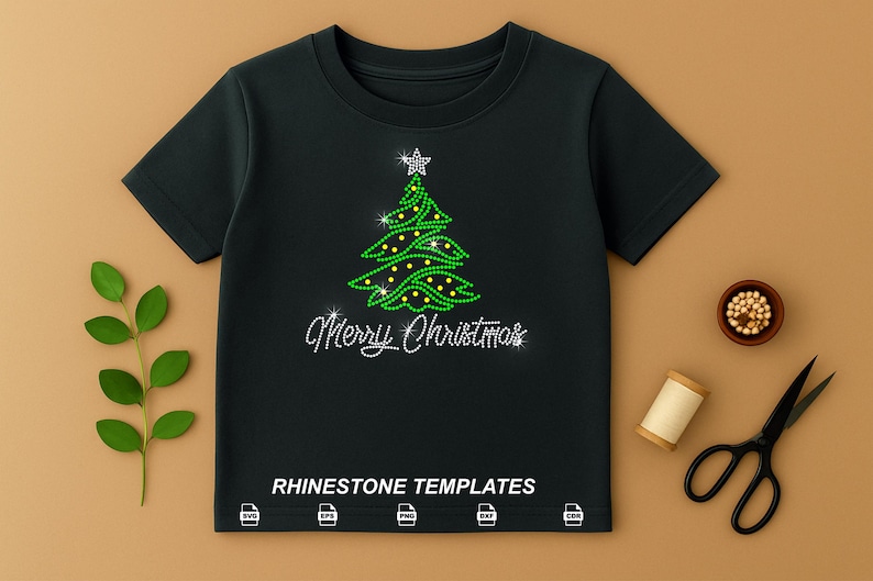 May include: Black t-shirt with a rhinestone Christmas tree design and the words "Merry Christmas". The tree is green with yellow accents and a star on top. The shirt is surrounded by a sprig of leaves, scissors, and other craft supplies.