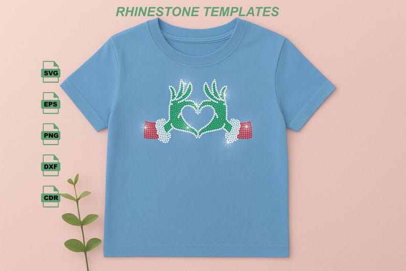 May include: A light blue t-shirt featuring a rhinestone design of green hands forming a heart shape. The hands have red and white accents. The text "RHINESTONE TEMPLATES" is at the top.