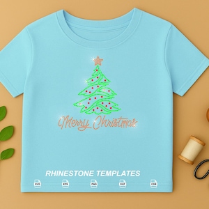 May include: A light blue t-shirt featuring a rhinestone graphic of a green Christmas tree with red ornaments and a gold star topper. Below the tree, the text Merry Christmas is written in gold rhinestones. The text RHINESTONE TEMPLATES is printed at the bottom with SVG, EPS, PNG, DXF, and CDR icons.