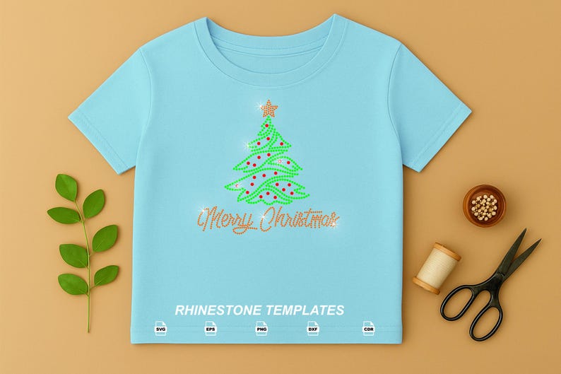 May include: A light blue t-shirt featuring a rhinestone graphic of a green Christmas tree with red ornaments and a gold star topper. Below the tree, the text Merry Christmas is written in gold rhinestones. The text RHINESTONE TEMPLATES is printed at the bottom with SVG, EPS, PNG, DXF, and CDR icons.