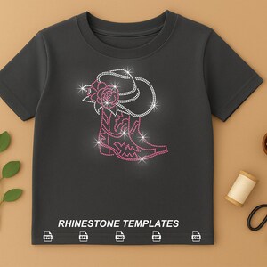May include: A dark gray t-shirt featuring a rhinestone design of a cowboy hat and boot. The boot and hat are outlined in white rhinestones with pink accents. The text "RHINESTONE TEMPLATES" is printed at the bottom.