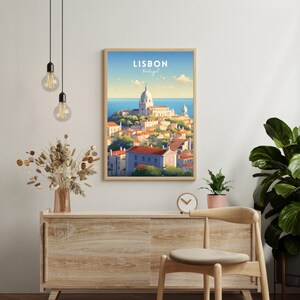 K&ouml;nnte beinhalten: Ein gerahmtes Poster mit einer farbenfrohen Illustration von Lissabon, Portugal. Das Poster zeigt eine Stadtlandschaft mit einer Kirche und Geb&auml;uden im Vordergrund und einem blauen Meer im Hintergrund. Der Text "LISBON Portugal" ist oben auf dem Poster in Wei&szlig; gedruckt.