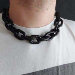 Può includere: Una collana spessa a catena nera composta da grandi ovali collegati. La collana è indossata da una persona, ma il viso della persona non è visibile.