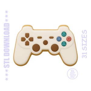 May include: A white and tan controller-shaped cookie with brown and colored button details. The cookie has a light brown outline. Text on the image says "STL DOWNLOAD" and "31 SIZES".