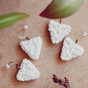 Puede incluir: Tres pares de pendientes triangulares de crochet blanco con ganchos dorados.