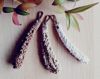 May include: Three handmade macrame keychains in brown, beige, and white. Each keychain has a silver metal ring and a small silver tag.