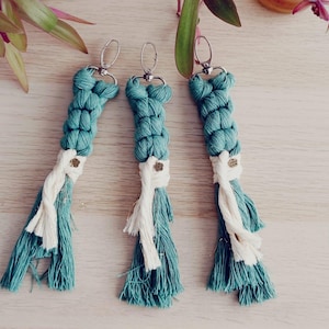 May include: Three teal blue and white braided keychains with a silver key ring. The keychains have a tassel at the bottom.