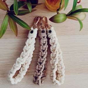 May include: Three braided keychains with gold metal clasps and black beads. The keychains are made of natural fiber rope in beige and brown.