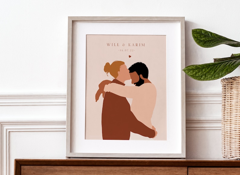 May include: A framed illustration of two people embracing. The couple is depicted in a minimalist style with brown and pink tones. The text "Will & Karim - 14.07.22" is printed below the illustration.