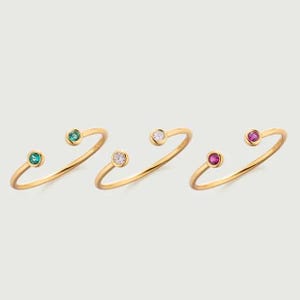 May include: Four gold rings with a single gemstone on each side. The rings feature green, white, and red gemstones.