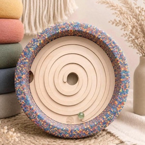 Könnte beinhalten: Ein Holz-Spiral-Labyrinth-Spielzeug mit einem bunten, perlenbesetzten Rand. Das Labyrinth hat eine hellgrüne Murmel und das Wort "HERRLICH" ist unten aufgedruckt. Das Spielzeug ist für das Spielen und die Entwicklung von Kindern konzipiert.
