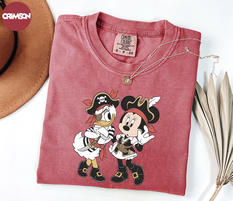 a red t-shirt with a cartoon image of Minnie Mouse and Donald Duck dressed as pirates, along with a necklace and a hat.