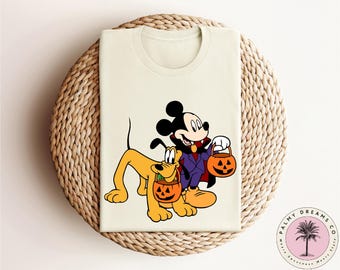 May include: A white t-shirt featuring a cartoon image of Mickey Mouse dressed as a vampire and Pluto holding a pumpkin. Mickey is holding a pumpkin in his other hand.