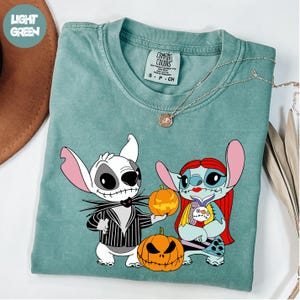 A t-shirt with a graphic design featuring two cartoon characters, a skeleton and a pumpkin, dressed in Halloween-themed outfits.