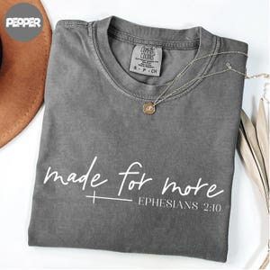 A gray t-shirt with the text "made for more" printed on it, along with a Bible verse reference "Ephlesiads 2:10".