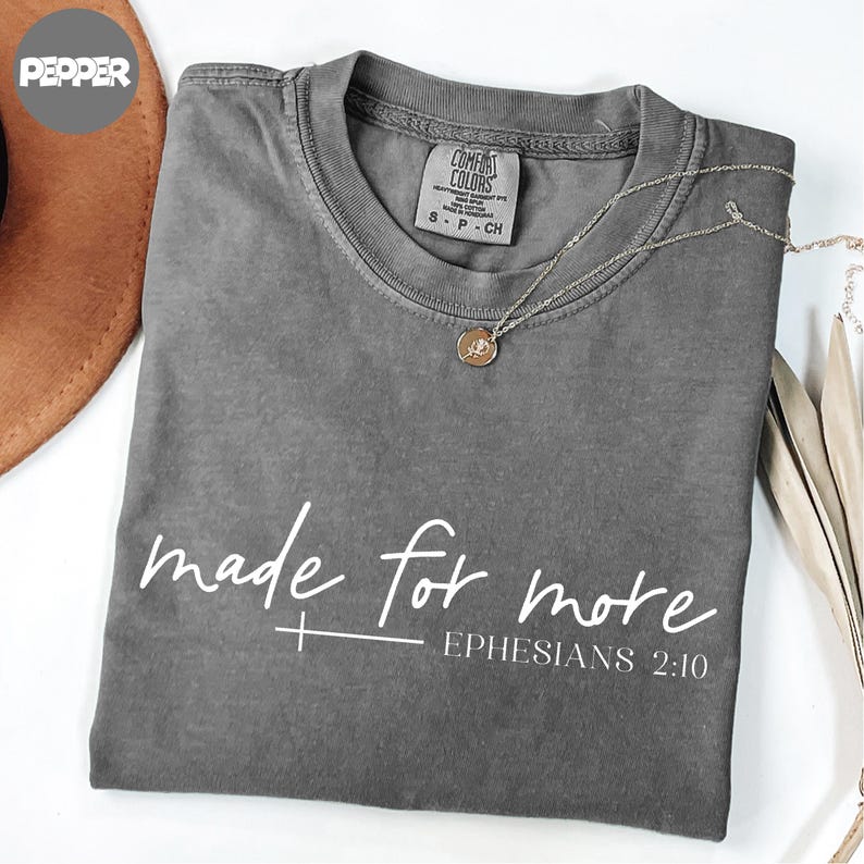 A gray t-shirt with the text "made for more" printed on it, along with a Bible verse reference "Ephlesiads 2:10".
