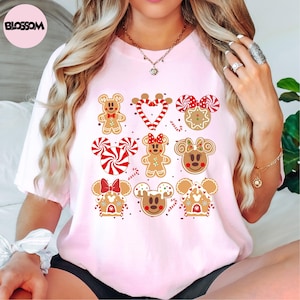 A woman wearing a pink t-shirt with a graphic design of various Disney characters and sweets, including Minnie Mouse, gingerbread men, and candy canes.