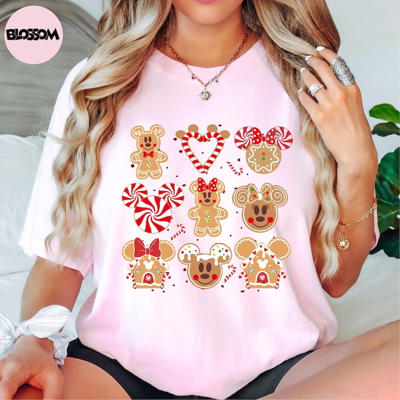 A woman wearing a pink t-shirt with a graphic design of various Disney characters and sweets, including Minnie Mouse, gingerbread men, and candy canes.