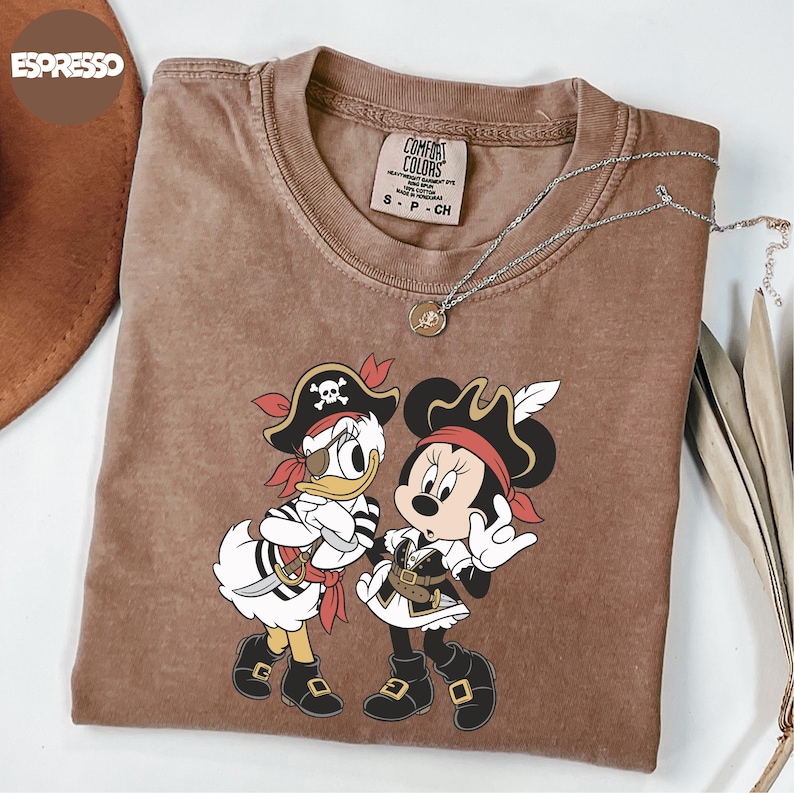 A brown t-shirt with a cartoon image of Minnie Mouse and Donald Duck dressed as pirates, along with a necklace and a hat.