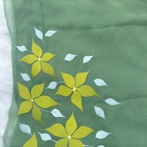 May include: A green fabric with a floral design. The flowers are yellow with white centers and are surrounded by white leaves.