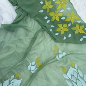 May include: A sheer green fabric with white and yellow floral designs. The fabric is draped over a white surface.