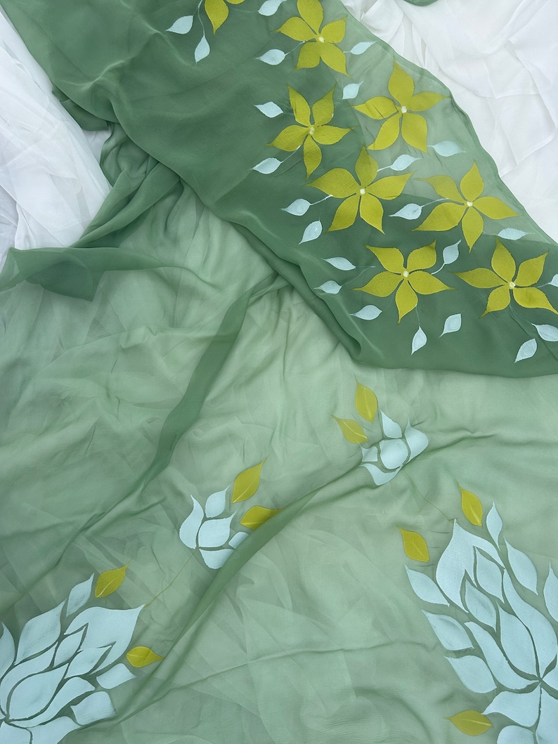 May include: A sheer green fabric with white and yellow floral designs. The fabric is draped over a white surface.