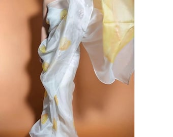 May include: A white sheer saree with yellow leaf-like patterns. The saree is draped over a person's body, with the end of the saree flowing in the air.