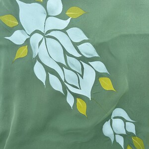 May include: A green fabric with a white floral design. The flowers are made up of multiple white petals with yellow leaves.